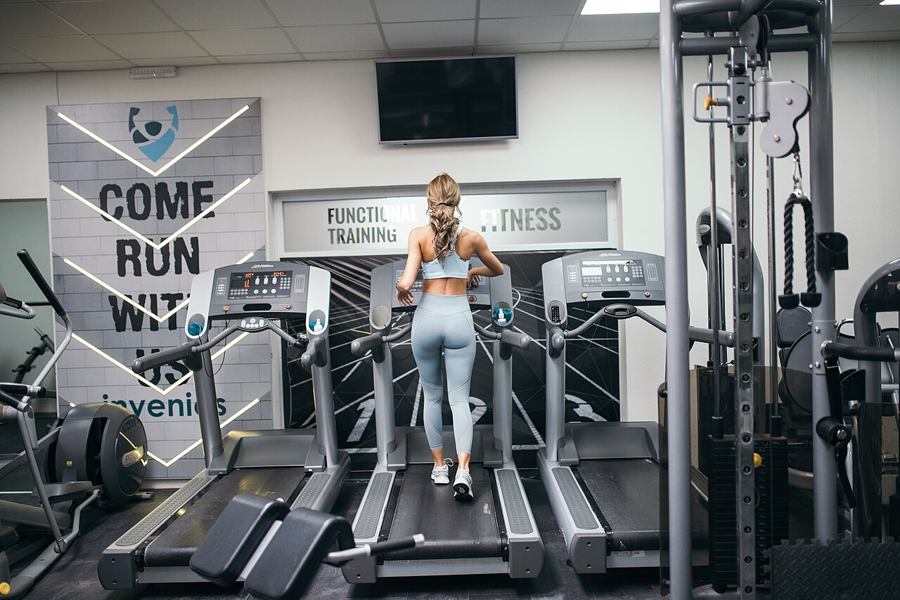 A woman in light grey leggings running on a treadmill in a gym