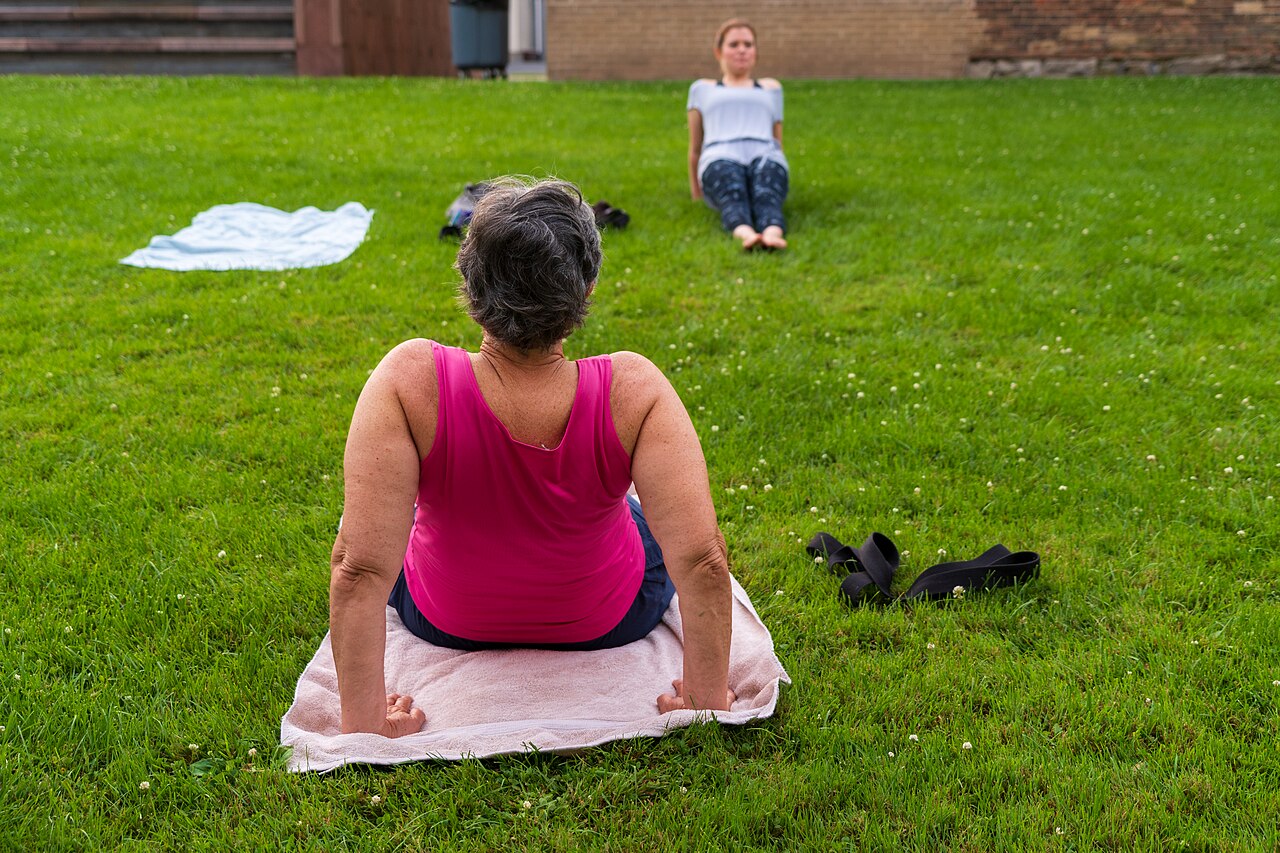 Women stretching on towels on a lawn during an outdoor yoga class
