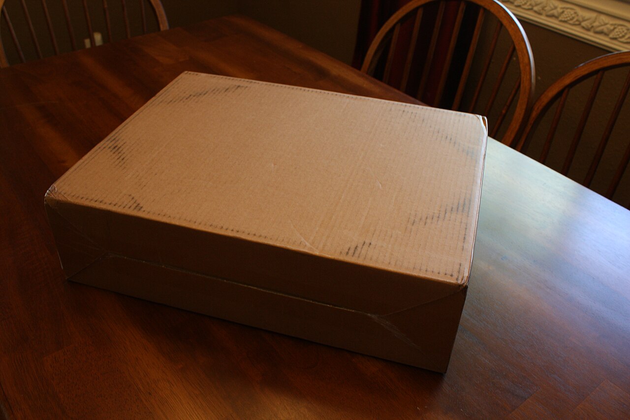A taped cardboard shipping box on a wooden dining table