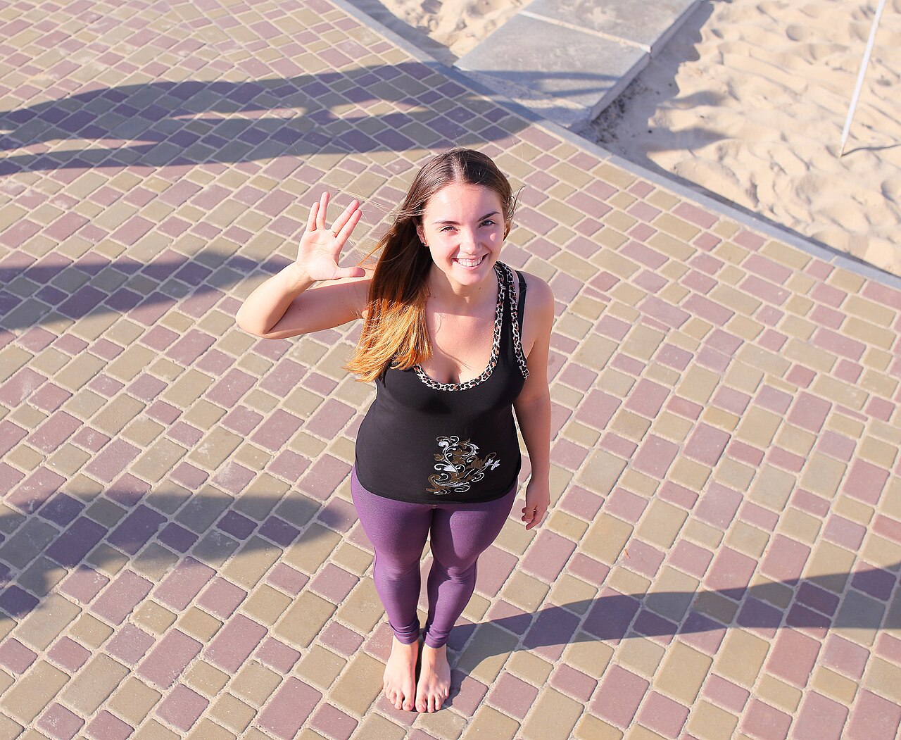 A woman in purple ankle-length leggings standing barefoot on a paved promenade